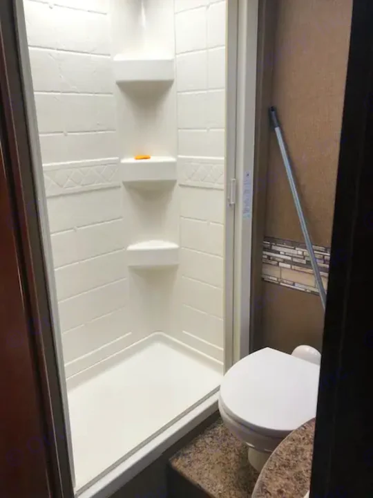 Compact RV rental bathroom features a white shower stall with shelves (with soap) and a toilet.. Thor Four Winds 2017