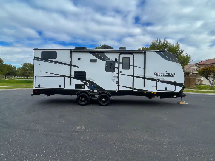 Modern white travel trailer, branded "North Trail Ultra Lite," ready for rv rental on an asphalt lot under a cloudy sky.. Heartland North Trail 2022