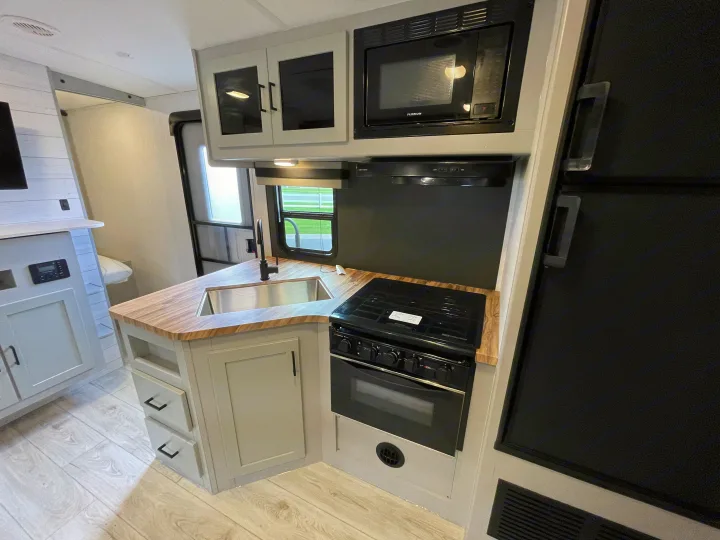 RV rental kitchen: modern interior with light wood counters, sink, gas range, oven, microwave, and gray cabinets.. Heartland North Trail 2022