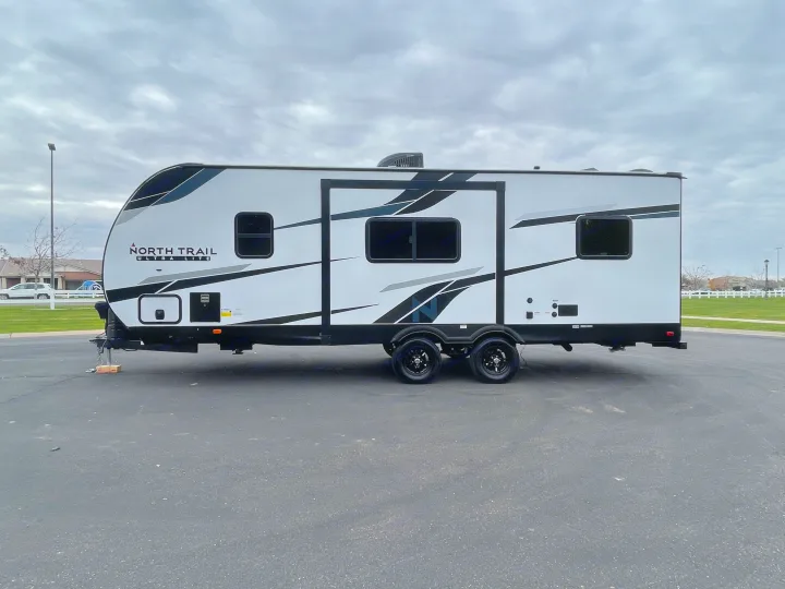 A sleek white and black North Trail travel trailer, perfect for an RV rental, parked on asphalt under a cloudy sky.. Heartland North Trail 2022