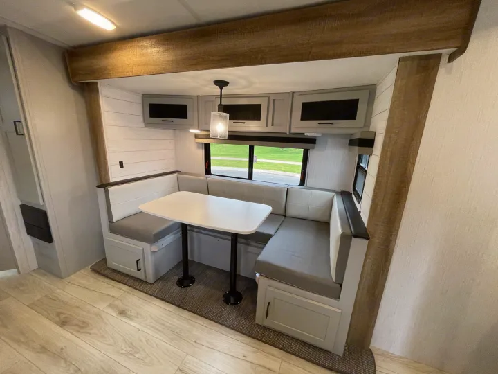 Modern RV rental interior: a bright dinette with U-shaped seating, table, overhead cabinets, and wood accents.. Heartland North Trail 2022