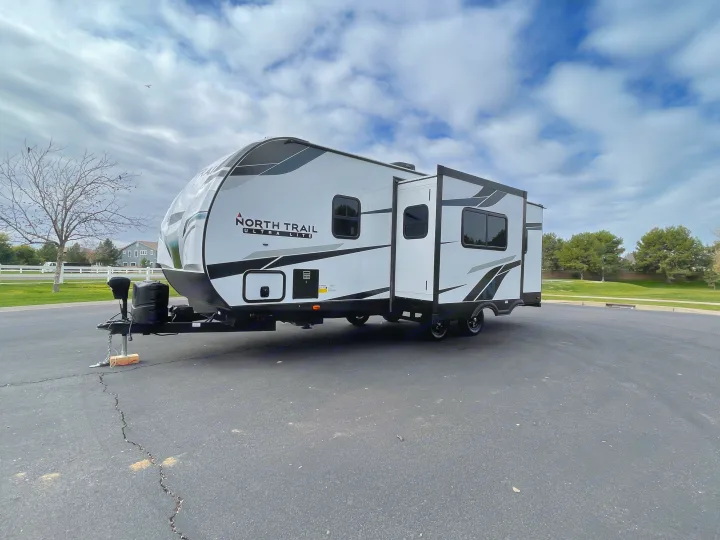 Modern white and black travel trailer RV rental, with slide-out extended, parked on asphalt. Ready for your outdoor adventures.. Heartland North Trail 2022