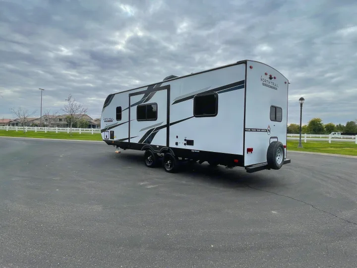 Spacious North Trail Ultra Lite travel trailer for RV rental, parked on asphalt under cloudy sky.. Heartland North Trail 2022