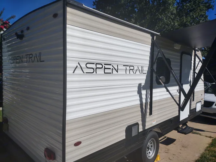 Side view of a parked Aspen Trail travel trailer with an extended awning, ideal for your RV rental trips.. Dutchmen 17BH 2021
