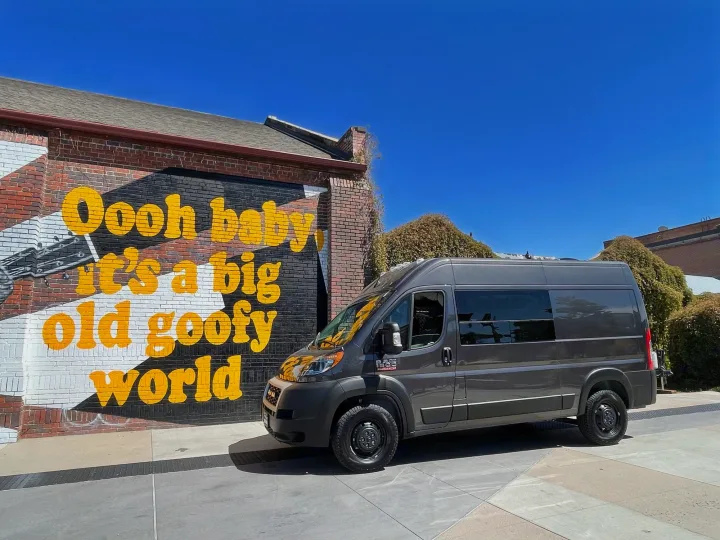 Gray Ram ProMaster RV rental van beside a "big old goofy world" mural. Perfect for exploring and travel adventures!. Ram Promaster 2022