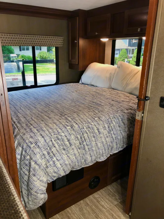 Cozy RV rental bedroom with a comfortable bed, large window, and wooden storage cabinets.. Forest River Sunseeker LE 2020