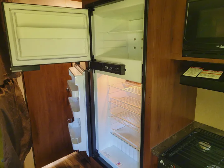 Inside an RV rental, an open, empty refrigerator with a microwave and stovetop visible, showcasing the compact kitchen.. Jayco Jay Flight SLX 2017