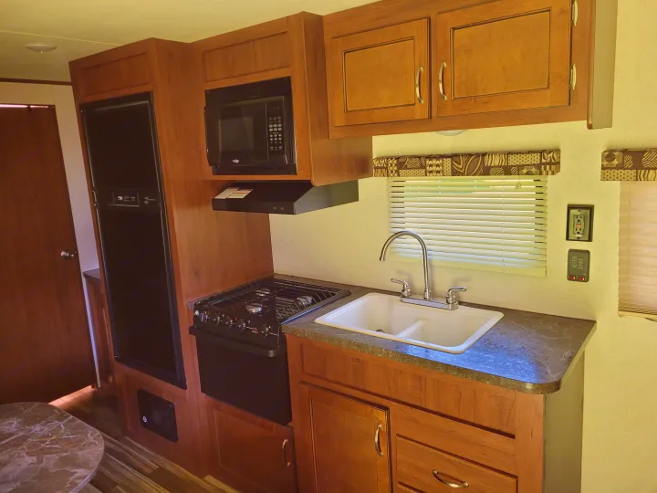 Compact RV rental kitchen featuring a fridge, microwave, gas stove, and double sink. Ideal for travel cooking.. Jayco Jay Flight SLX 2017
