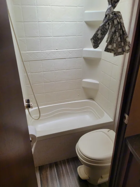 RV rental bathroom with a white shower-tub combo, toilet, and patterned curtain, showing a clean, functional space.. Jayco Jay Flight SLX 2017
