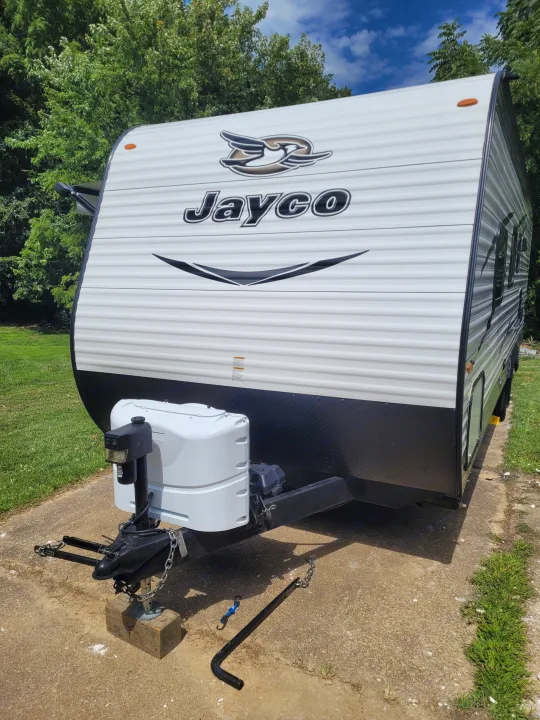 This white Jayco RV rental, a travel trailer, is parked on a concrete pad, ready for your next adventure amidst green trees.. Jayco Jay Flight SLX 2017