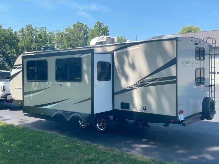 A light-colored Starcraft Super Lite RV rental, with its slide-out extended, sits on a paved driveway under a blue sky.. Starcraft Super Lite 2022