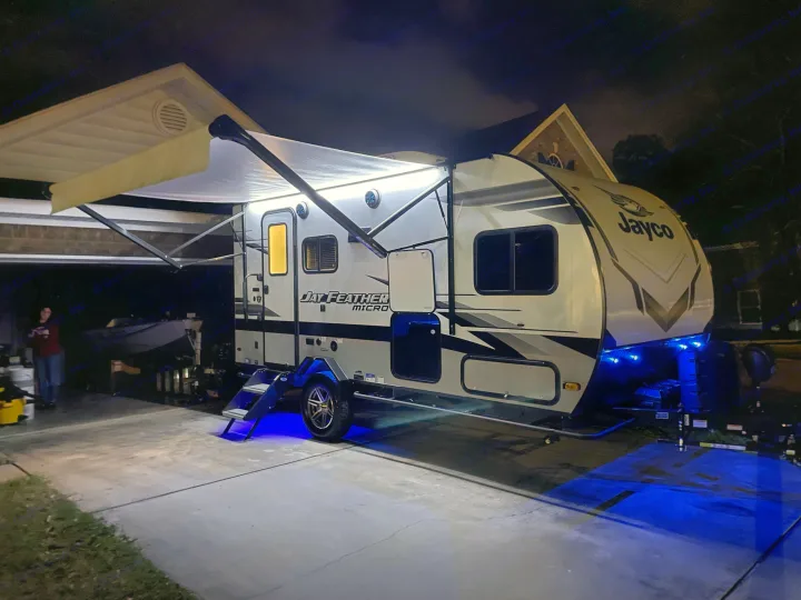 A modern Jayco travel trailer RV rental brightly lit at night with white awning and blue ground lights.. Jayco Jay Feather Micro 2022