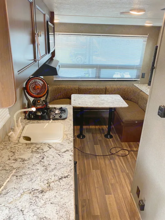 Experience this RV rental interior: well-equipped kitchen with portable stove, sink, and U-shaped dining booth. Adventure awaits!. Keystone RV Hideout LHS Mini 2018