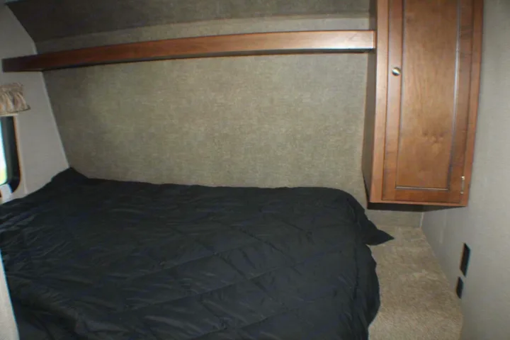 Cozy RV rental bedroom features a comfy black bed, overhead shelf, and wall-mounted cabinet, perfect for your travels.. Keystone RV Hideout LHS Mini 2018