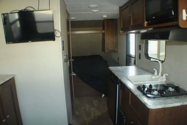 Explore this functional rv rental interior: kitchen with sink & stove, microwave, TV, and a cozy bedroom area.. Keystone RV Hideout LHS Mini 2018