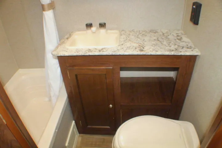 Compact RV rental bathroom features a white tub, sink vanity with wood cabinets, and a toilet.. Keystone RV Hideout LHS Mini 2018