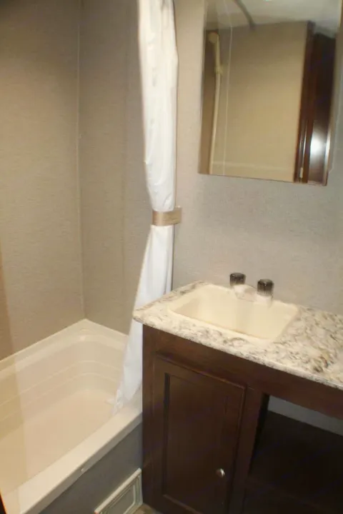 Compact RV rental bathroom showcasing a practical shower/tub, vanity with sink, and mirror.. Keystone RV Hideout LHS Mini 2018