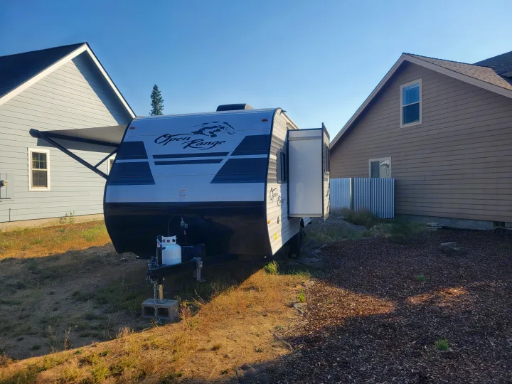 An Open Range RV rental with awning & slide-out extended, parked between two houses on a sunny day.. Highland Ridge RV Open Range 2022