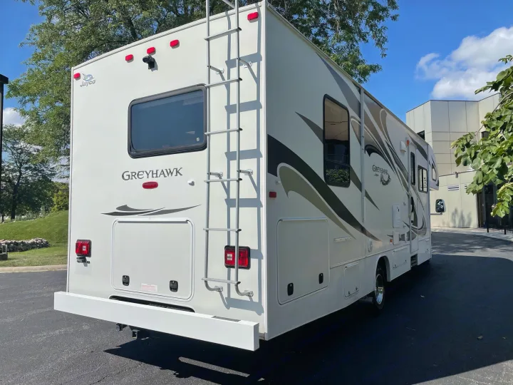 Jayco Greyhawk RV rental parked on asphalt. View of its rear and side with ladder, windows, and storage.. Jayco Greyhawk 2013