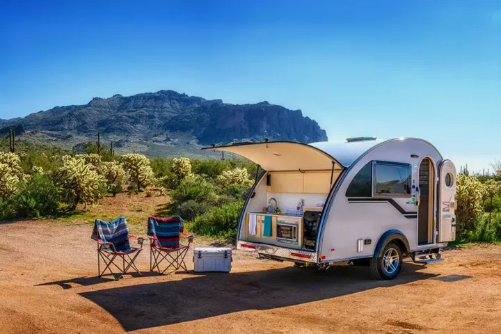 RV rental ready for adventure: Teardrop trailer with open kitchen, chairs, & desert mountains.. Nucamp TAB 320 CS-S 2022
