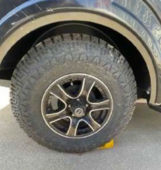 Rugged tire and black/silver wheel of an RV rental, safely secured by a yellow chock block on asphalt.. Nucamp TAB 320 CS-S 2022