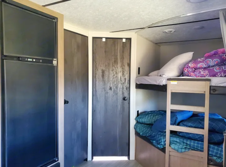 Cozy RV rental interior featuring a refrigerator, two dark doors, and practical bunk beds for family travel and compact living.. Keystone RV Hideout 2021