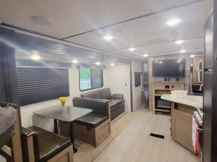 Spacious RV rental interior with dining booth, sofa, kitchen, TV, and bunk beds.. Keystone RV Hideout 2021