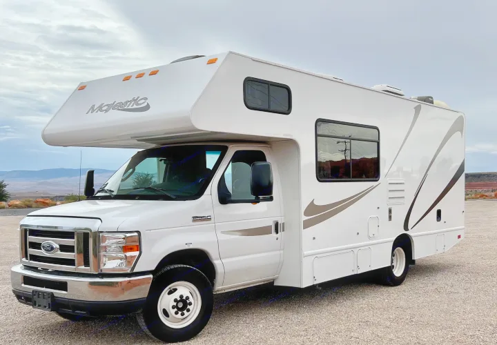 This clean white Majestic Class C RV rental is parked on a gravel lot with distant mountains, ready for adventure.. Thor Majestic 2018