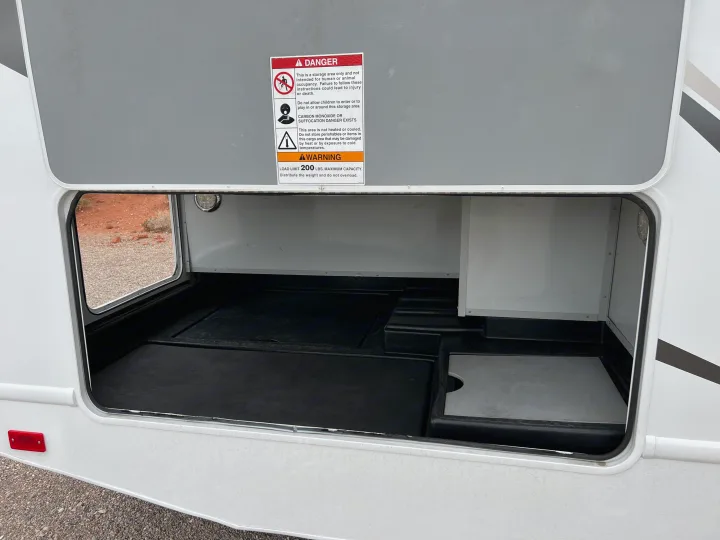 RV rental: Open external storage bay with safety warnings about human/animal occupancy, temperature, and a 200 lbs load limit.. Thor Majestic 2018