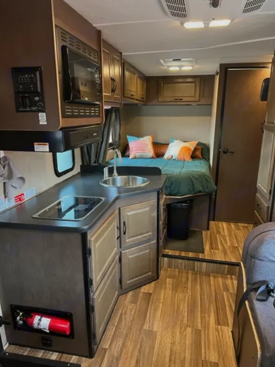 This RV rental interior features a compact kitchen with microwave and sink, and a comfortable bed area.. Thor Majestic 2018
