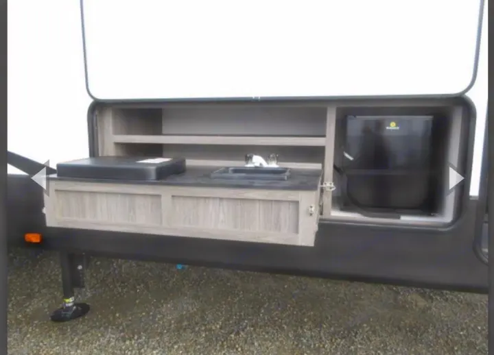 Convenient outdoor kitchen in an RV rental, showing a sink, mini-fridge, and covered cooking surface.. Crossroads RV Volante HP 2022