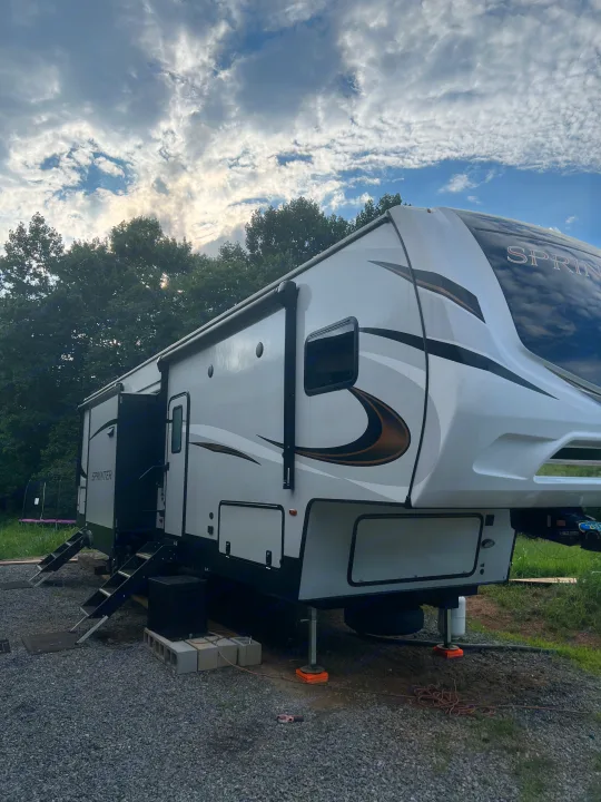 This beautiful fifth-wheel RV, perfect for an RV rental adventure, is set up at a scenic campsite.. Keystone RV Sprinter Campfire Edition 2021