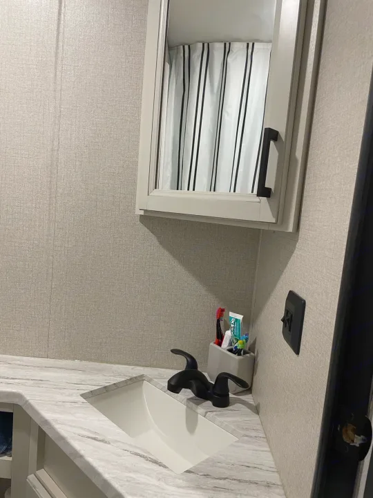 Modern RV rental bathroom vanity with sink, black faucet, toothbrush holder, and mirror reflecting a striped shower curtain.. Highland Ridge RV Olympia 2022