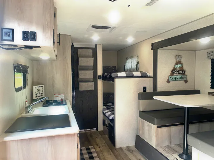 Cozy RV rental showcasing a modern kitchenette, two bunk beds, and a dinette. Light wood tones, black and white decor.. K-Z Manufacturing Sportsman Classic 2022