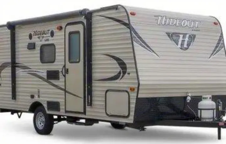 Light-colored Hideout travel trailer, perfect as an RV rental, with an awning, door, and propane tanks visible.. Keystone RV Hideout LHS Mini 2018