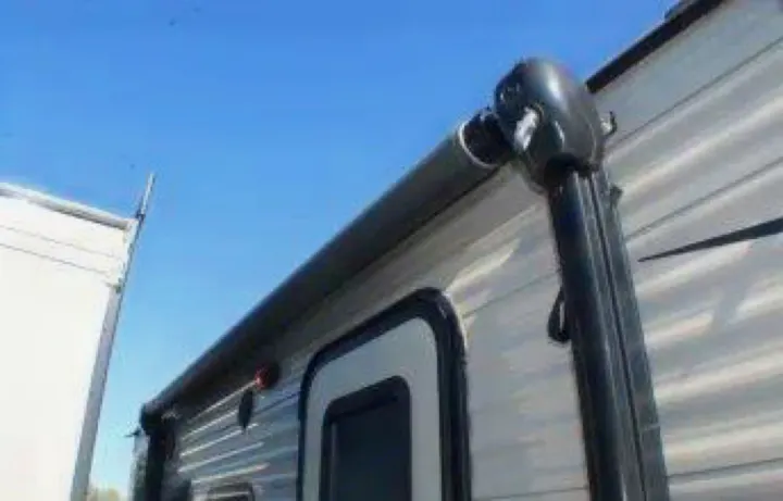 Close-up of an RV rental showing its rolled-up awning and side door under a clear blue sky, ready for adventure.. Keystone RV Hideout LHS Mini 2018