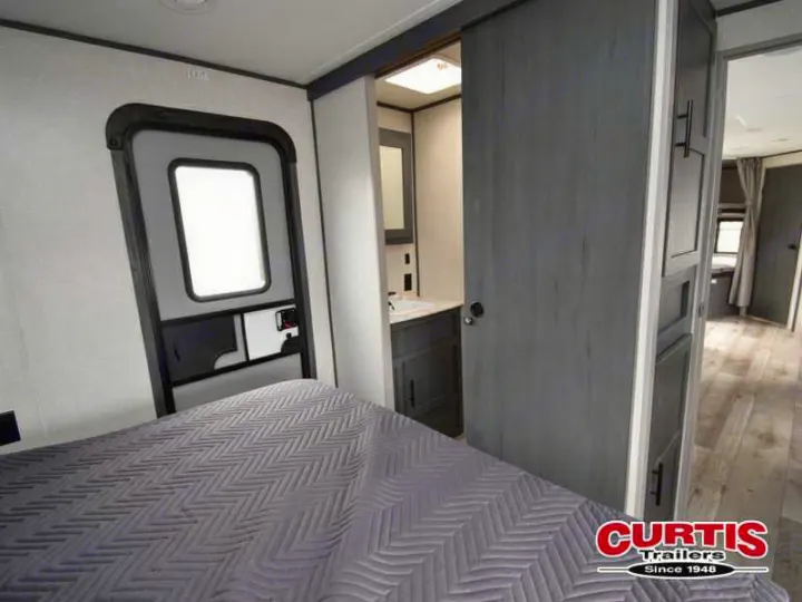 RV rental interior: A compact bedroom with grey bed, exit door, and sliding door to the bathroom.. Aspen Trail Aspen Trail Trailer 2021