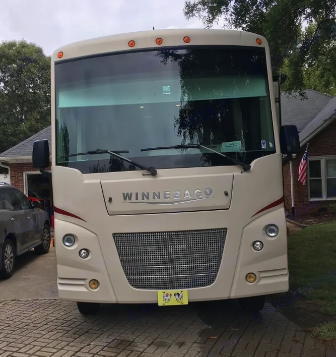 A cream Winnebago motorhome (RV) is parked head-on in a brick driveway with a house in the background, ready for rv rental.. Winnebago Vista 2017