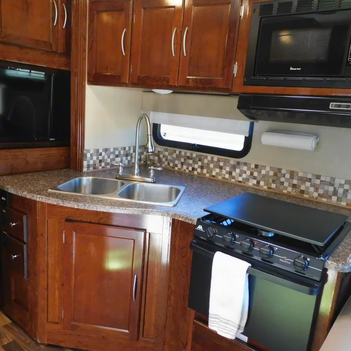 RV rental kitchen: Dark wood cabinets, double sink, gas stove, microwave, and TV visible. Fully equipped for your travels.. Coachmen Pursuit 2017