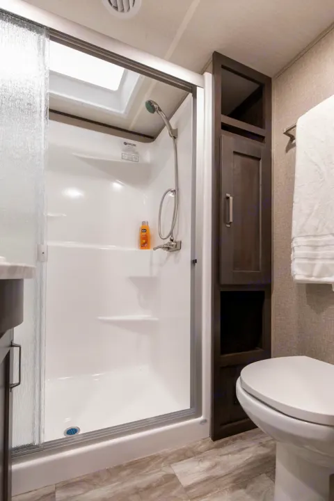 Step into this clean RV rental bathroom featuring a bright shower with skylight, smart storage, and a neat toilet area.. Grand Design Reflection 2021