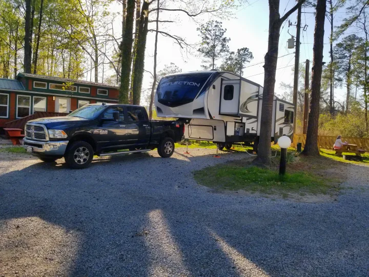 Sunny campground scene featuring a fifth-wheel RV rental towed by a truck, with a person relaxing nearby.. Grand Design Reflection 2021