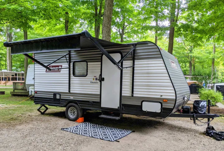 An RV rental, a Coleman travel trailer, is parked at a serene campsite with its awning extended, ready for a nature escape.. Coleman Coleman Lantern 2022