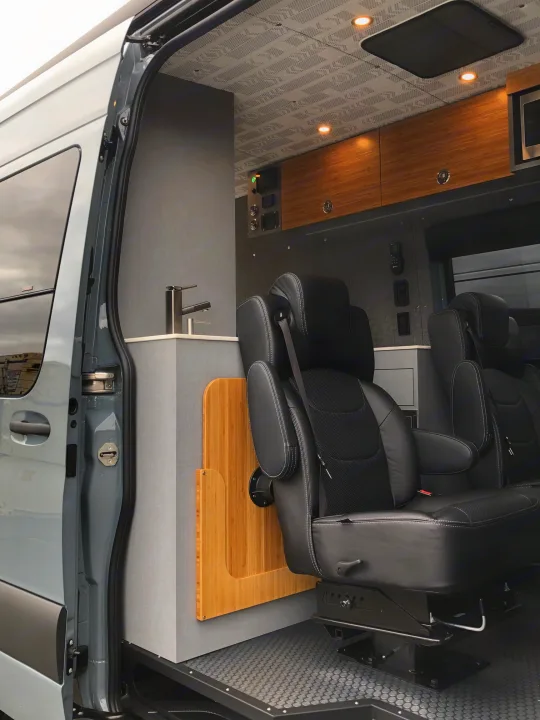 Luxury RV rental interior: spacious camper van with multiple black leather seats, wooden cabinetry, modern design.. Mercedes Sprinter 2022
