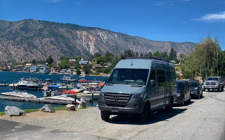 Gray Mercedes-Benz Sprinter RV rental parked by a bustling lake marina, surrounded by scenic mountains and lakeside homes.. Mercedes Sprinter 2022