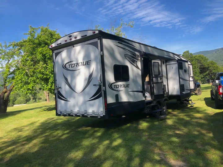 Spacious Torque RV rental parked on a sunny grassy field with trees & mountains. Perfect for camping adventures.. Heartland Torque 2017