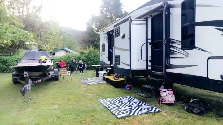 Enjoying an RV rental with friends! Large white RV and boat parked on grass, people relaxing in chairs at a campground.. Heartland Torque 2017