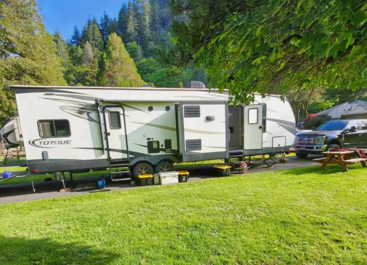 Enjoy nature with this large RV rental, a Torque travel trailer, parked at a sunny campground with a truck and picnic table.. Heartland Torque 2017