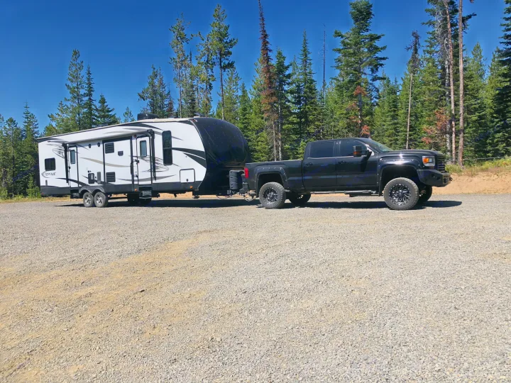 Black pickup truck towing a white travel trailer on gravel. Perfect for an RV rental adventure in the forest.. Heartland Torque 2017