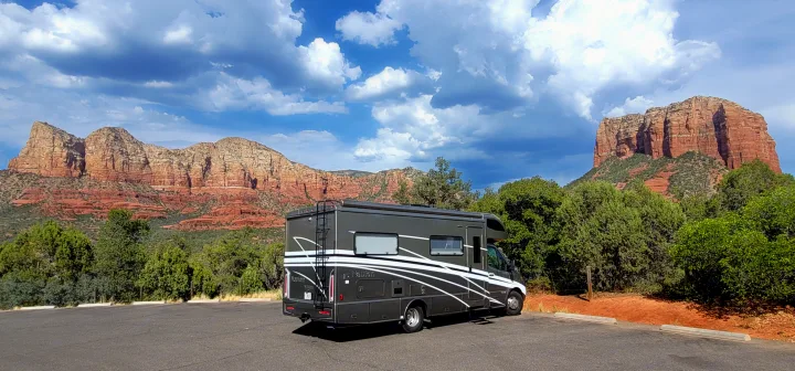 Dark gray RV rental parked against majestic red rock mountains and lush green trees under a cloudy sky.. Winnebago Navion 2022