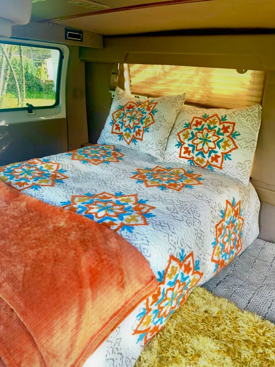 Cozy RV rental interior with a comfy bed, white and colorful mandala bedding, and a scenic window view.. Dodge Ram 1500 1999